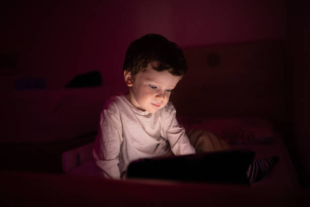 istock Little boy sitting in the dark room and using digital tablet 1351337446