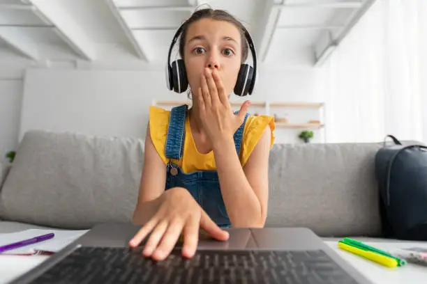 Photo of Surprised girl sitting at desk, having video call wearing headset