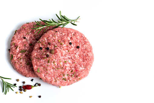 Two raw burgers with fresh spices on a white background isolated.