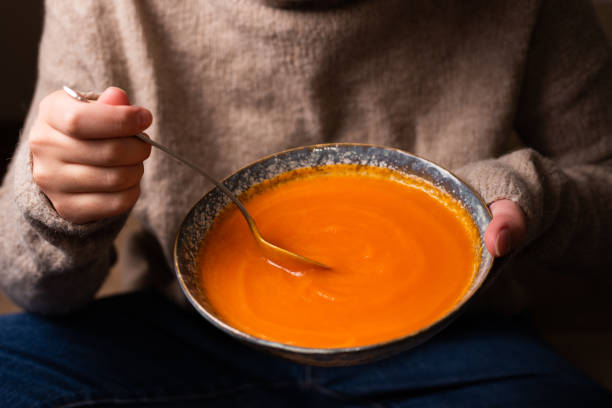 istock Female hand picking up pumpkin cream soup from a plate with a spoon. 1351338236