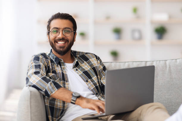 istock Positive indian guy reclining on couch with laptop 1351342354