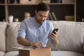 Happy young man unpacking parcel, leaving review in mobile app.