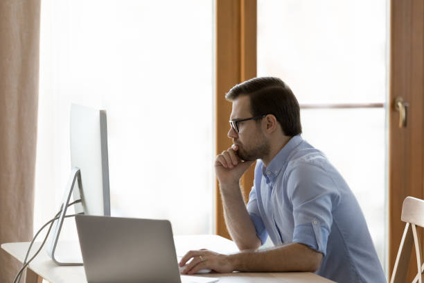 istock Pensive young businessman in eyewear working on computer. 1351342478