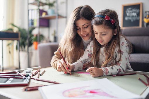 A young mother and her cute little daughter drawing with colorful pencils and having fun at home