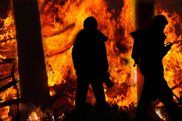 Silhousettes  of firefighters in a wildfire with burning trees.