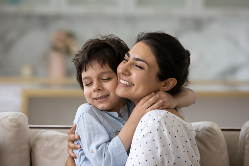 Sincere loving young asian indian woman cuddling cute little kid son, showing tender feelings. Happy two generations mixed race family enjoying sweet weekend moment together, relaxing at home.