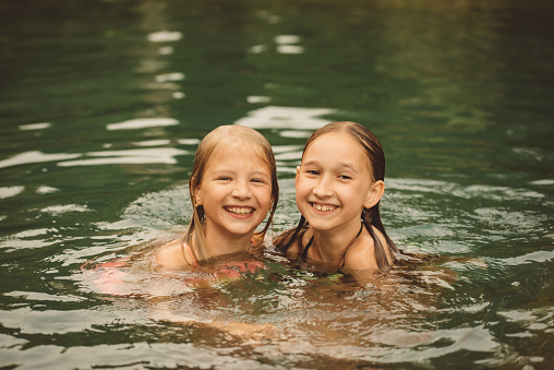 Two little girls are swimming in the pond. Children swim in the pool on a warm summer day. Healthy lifestyle concept. Portrait of happy girls floating in the lake.