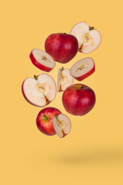 istock Minimal fruit idea with fresh sliced and whole apple floating in the air isolated on pastel yellow background. 1351348714