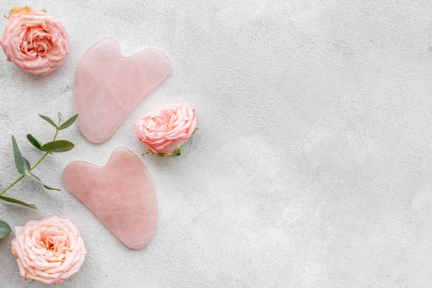 Pink gua sha massage stone with rose flowers for lifting face and wellness stock photo