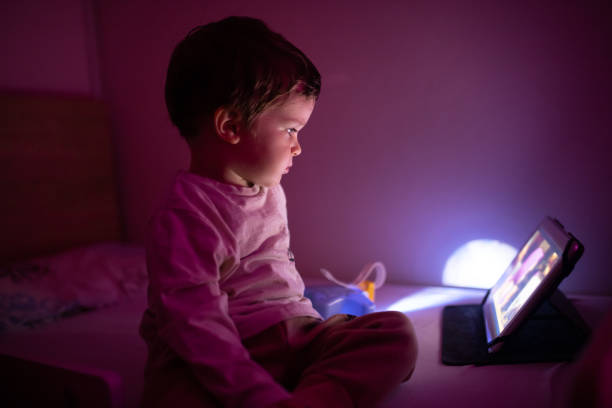 istock Little boy sitting in the dark room and using digital tablet 1351351619