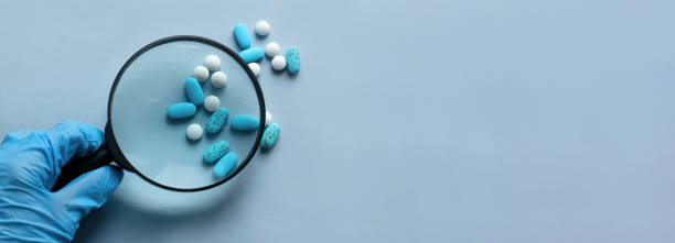 istock Doctor's workplace. Top view on a light background with scattered pills. A doctor in blue medical gloves holds a magnifying glass in his hand. Medical concept. 1351351675