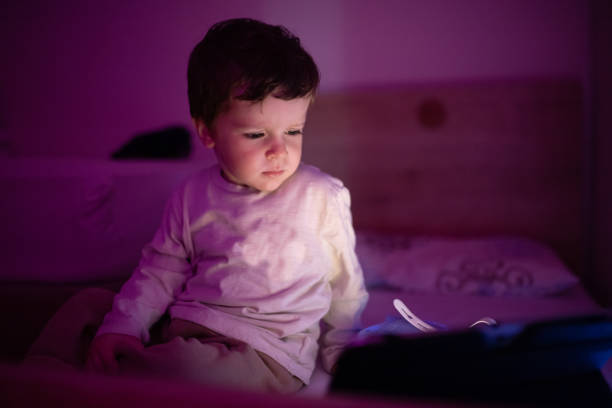 istock Little boy sitting in the dark room and using digital tablet 1351351677