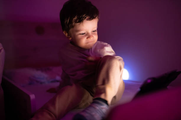 istock Little boy sitting in the dark room and using digital tablet 1351352199