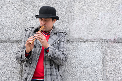 A man plays a musical instrument sopilka on the street against the background of the wall.