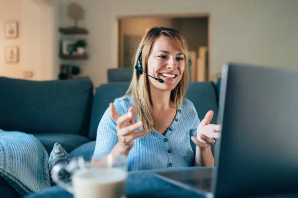 Shot of a young woman using a laptop and headset while working from home, having customer support video call