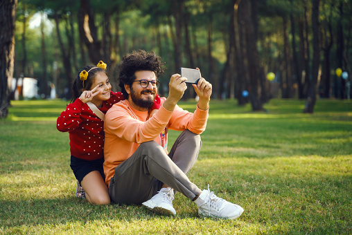 A father takes a selfie of him and his daughter while sitting at a public park, Antalya, Turkey