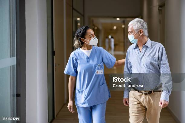 Doctor Talking To A Patient In The Corridor Of A Hospital While Wearing Face Masks Stock Photo - Download Image Now