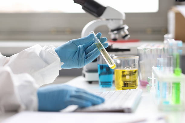 istock Gloved scientist holds test tube with transparent liquid and types on keyboard 1351405800