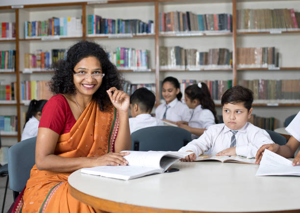istock Teacher helping students writing in book at school library 1351410823