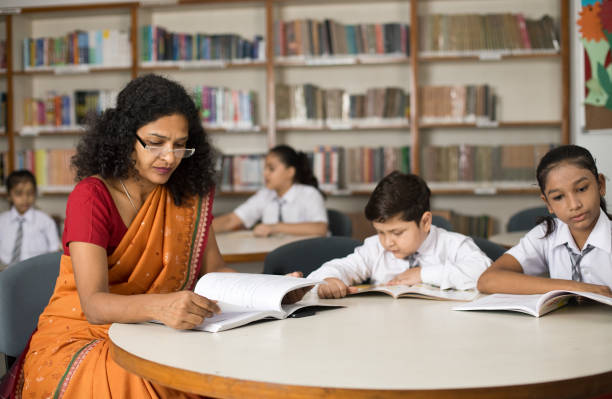 istock Teacher helping students writing in book at school library 1351410882