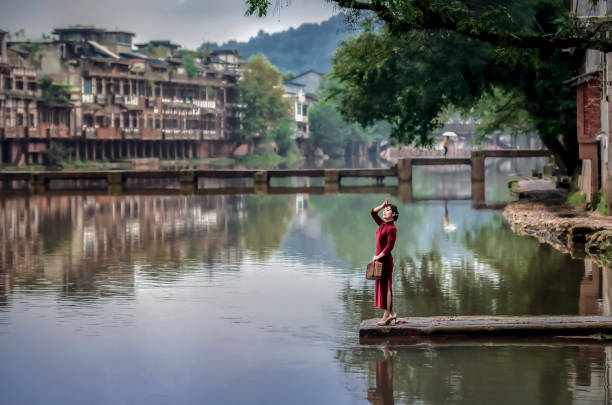 A woman with a suitcase stands by a river waiting for a boat in the ancient town of Jiaguan in Chengdu, China