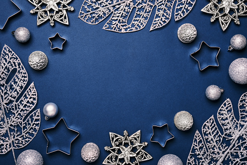Christmas blue background. Shining silver pattern frame made of frost decorative leaves and baubles.