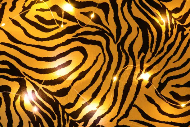 Photo of Blurred background. Luminous garland on tiger cloth,  flat lay. Symbol 2022 Tiger