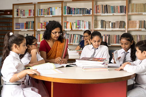 Female teachers teaching students in library at school