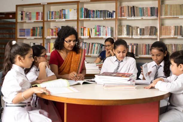 Female teachers teaching students in library at school stock photo
