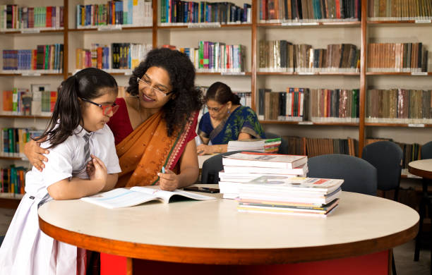istock Teacher helping schoolgirl studying in library 1351416196