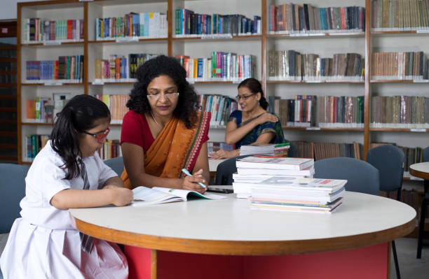 istock Teacher helping schoolgirl studying in library 1351416209