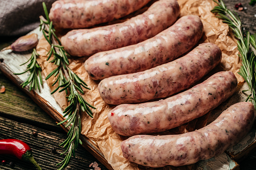 raw sausages with rosemary on a wooden background. Sausages for grilling. Food recipe background. Close up.