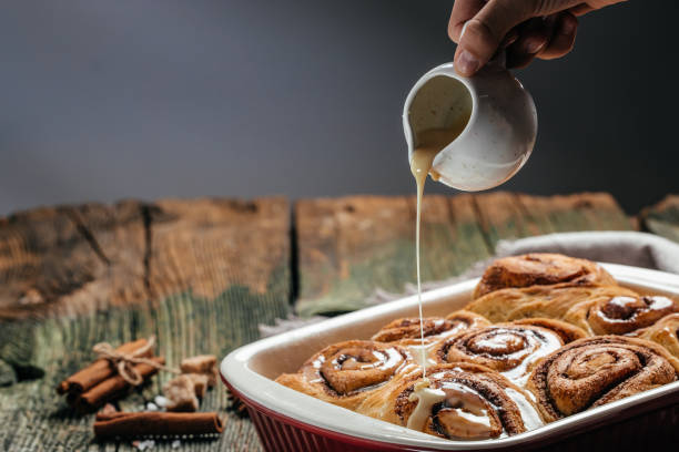 istock Homemade Cinnamon roll. Woman's hand spreading vanilla icing freshly baked cinnamon rolls 1351417241