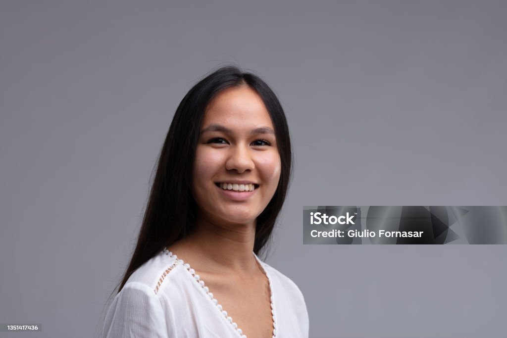 Happy young woman with a genuine warm smile Happy young woman with a genuine warm friendly smile in a head and shoulders view on grey Indigenous Peoples of the Americas Stock Photo