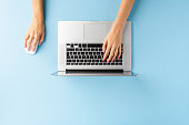 Overhead shot of female hands using laptop on blue office desktop. Business background. Flat lay
