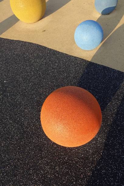 istock Orange stone ball with grain textured surface. Yellow and blue balls on the back. Black or graphite artificial floor background. Shadows on a sunny day. Reidi tee, Tallinn, Estonia 1351420229