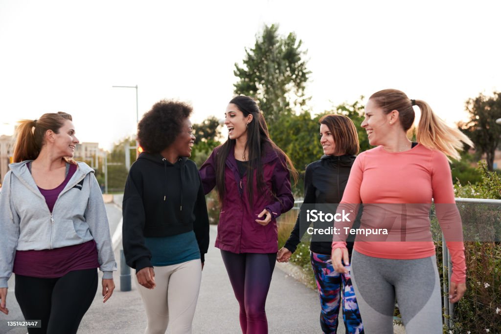 A group of women walking and talking after doing some outdoor exercise. Three-quarter length view of a group of women walking and talking in sportswear. Walking Stock Photo