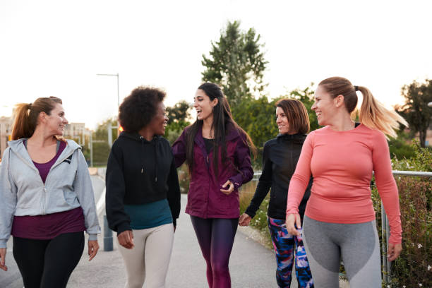 A group of women walking and talking after doing some outdoor exercise. Three-quarter length view of a group of women walking and talking in sportswear. Woman stock pictures, royalty-free photos & images