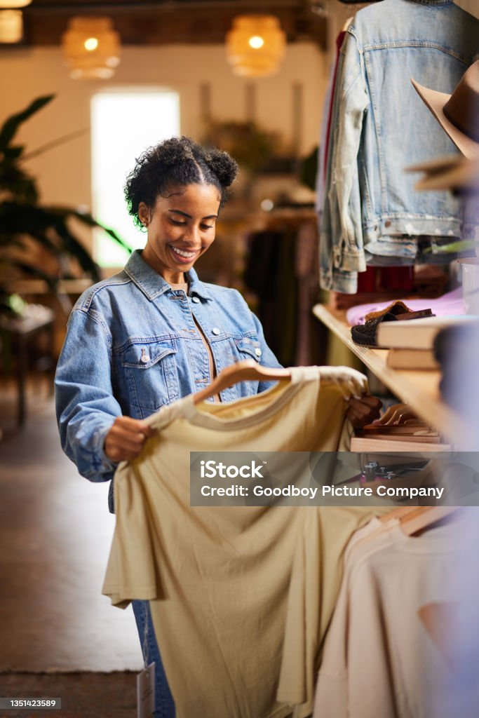 Smiling woman looking at shirt while shopping in a clothing store Young woman looking at a shirt and smiling while browsing the racks in a clothing boutique Retail Stock Photo