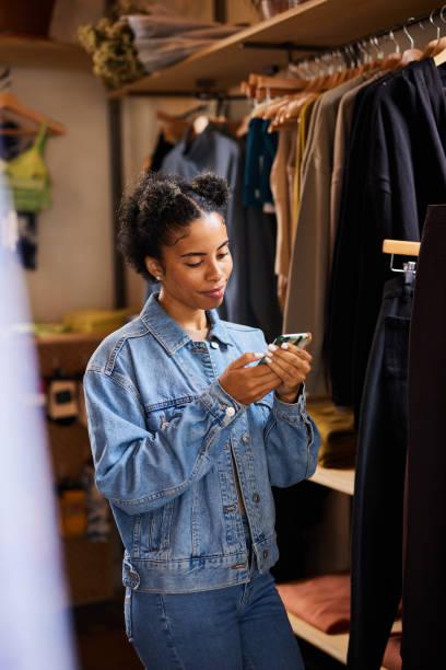 istock Smiling woman checking her phone while clothes shopping in a boutique 1351424821