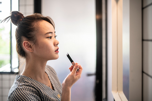 Asian chinese girl applying make-up in front of mirror
