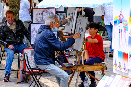 Montmartre, Paris, France - 15.07..2021: painter drawing a portrait of a kid on Place du Tertre on Montmartre district in Paris, France