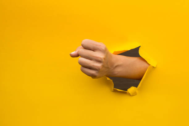 istock Woman's fist through broken paper 1351430388