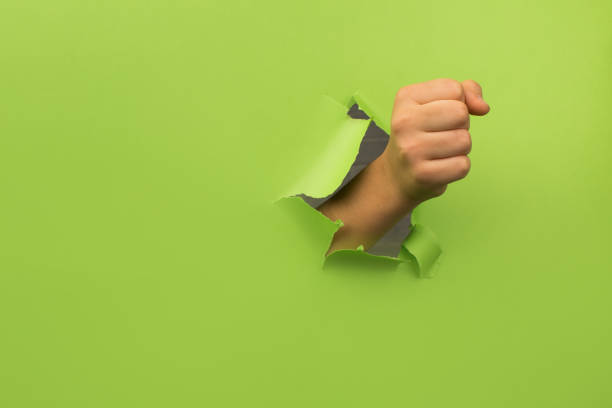 istock Woman's fist through broken paper 1351430543