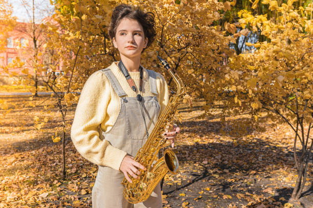 Portrait of a teenage girl with brown curly hair with a saxophone in her hands in an autumn park. Autumn saxophone melody. Children artists musicians creative personality