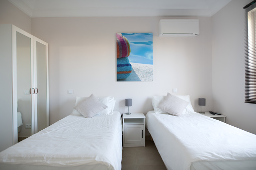 Clean twin bedroom in a house with white bed linen and white walls wardrobe with mirrored doors