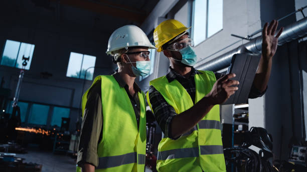 istock Industrial inspectors with face masks doing general check up at metal workshop, coronavirus concept 1351435361