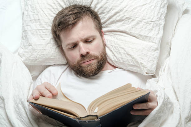 istock Attractive bearded man reading a book while lying in bed. Education concept. Top view. 1351436745