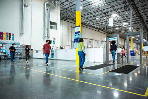 A line of people lined up to go through a metal detector at the entrance of a fulfillment center.