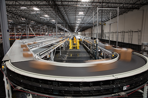 Packages blur as they rush past on the complex conveyor belt system that sorts them for delivery at a large fulfillment center.